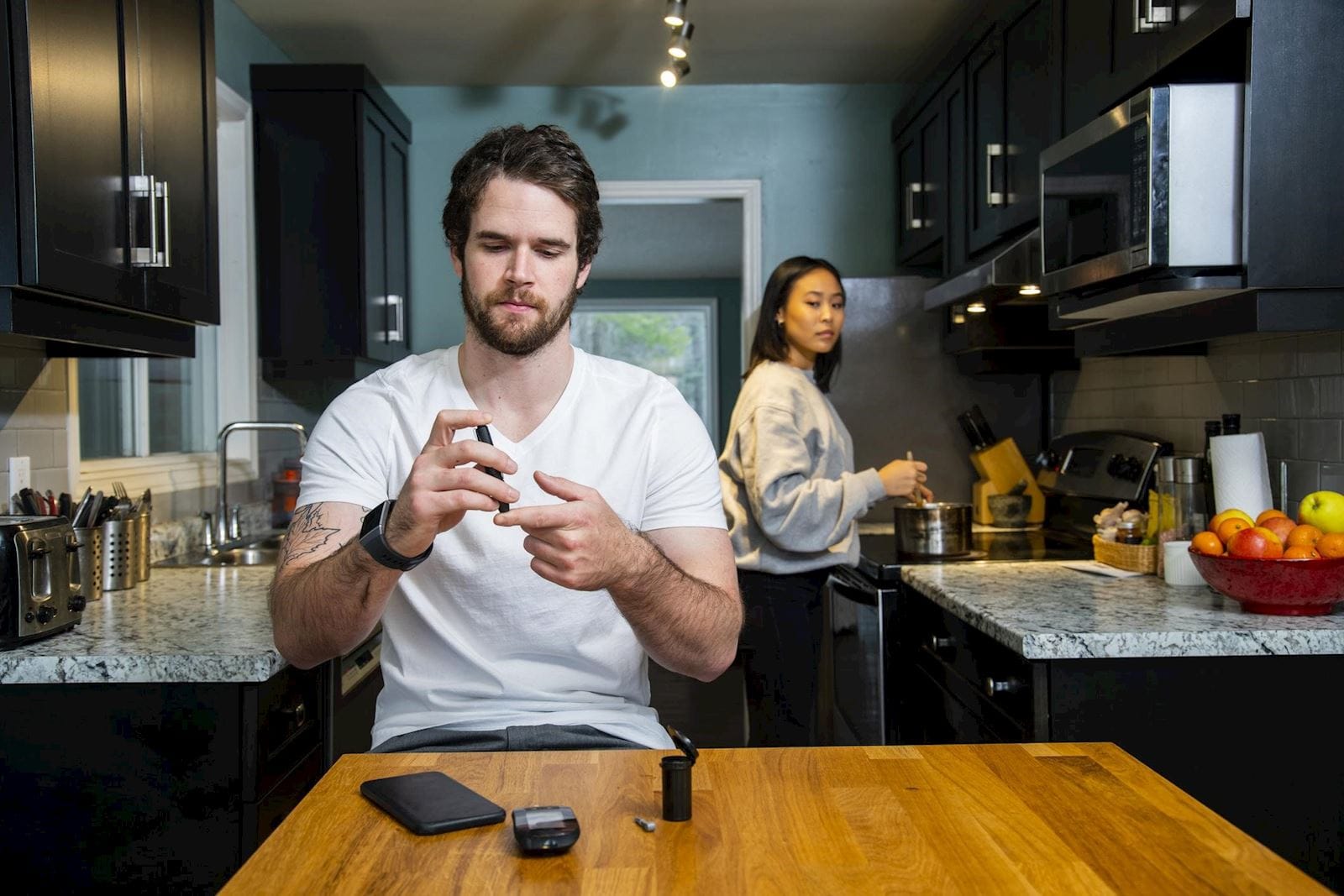 Man with diabetes checks his blood sugar with a finger prick while sitting in his kitchen